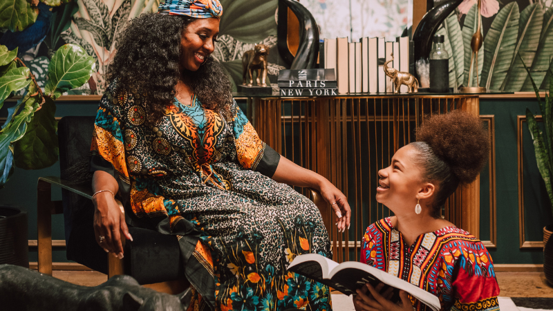 Black woman and young girl happily reading a book